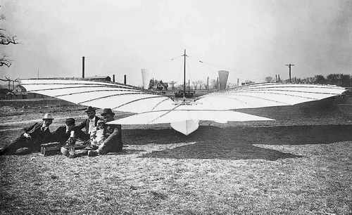 Gustav Wei&szlig;kopf (rechts) 1901 mit Tochter Rose auf seinem Scho&szlig; neben seinem Flugzeug Nr. 21. Vor ihnen der Motor, der die R&auml;der des vorderen Fahrwerks antrieb. Die Flugmaschine hatte eine Tragfl&auml;chenspannweite von 10,6 Meter.