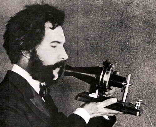 Ein Schauspieler portr&auml;tiert Alexander Graham Bell, wie er in ein fr&uuml;hes Modell seines Telefons spricht. Szene aus einem 1926 ver&ouml;ffentlichten Werbefilm der American Telephone & Telegraph Company (AT&T)